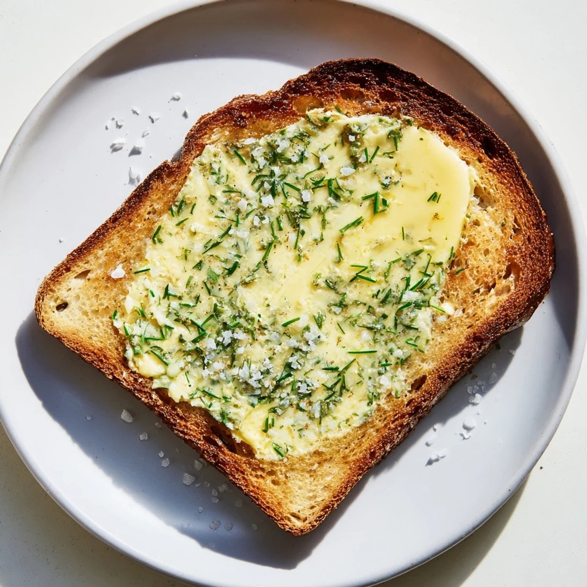 Close-up of golden Herb Butter Toast, with melted herbed butter pooling on crusty bread and a sprinkle of flaky salt.  