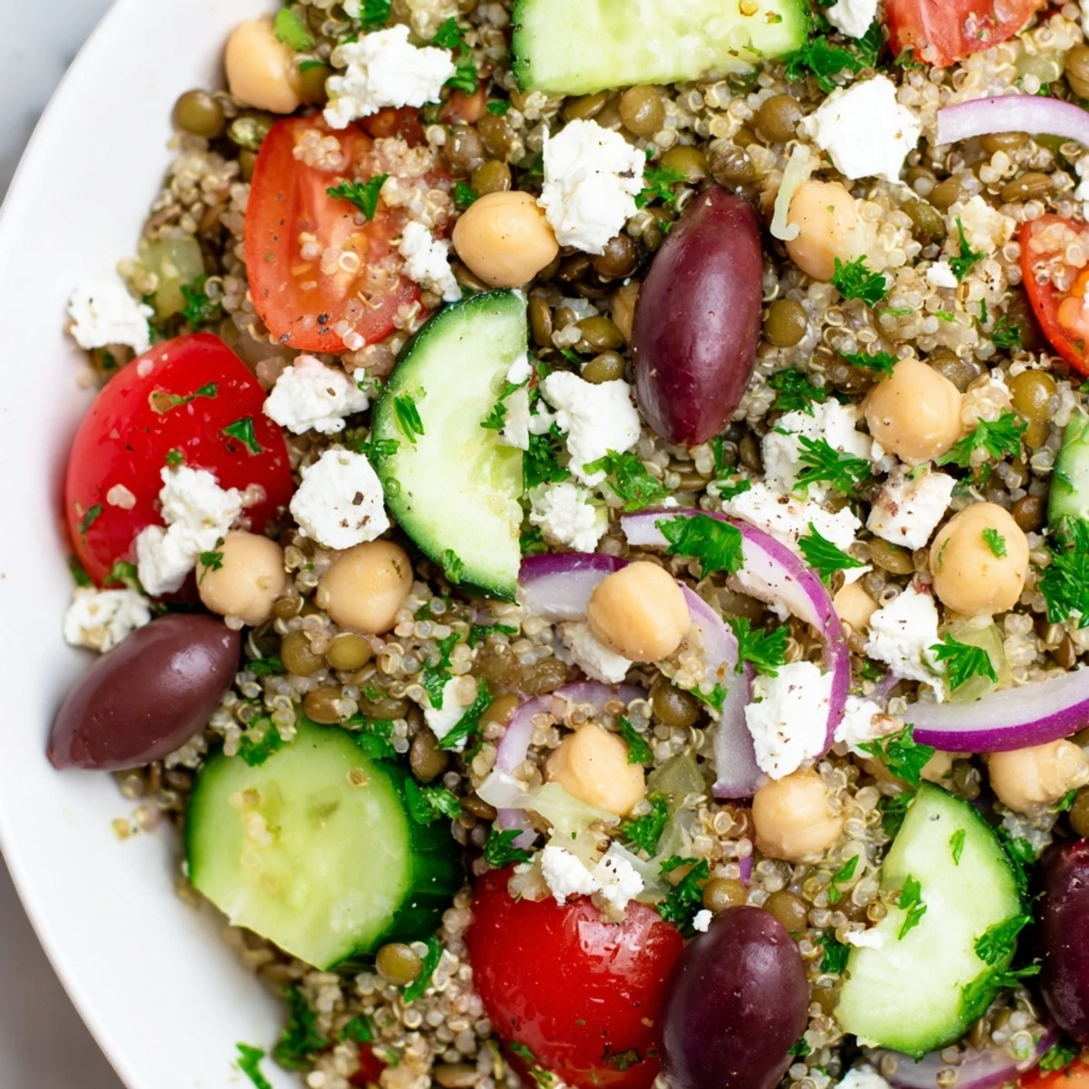A close-up of the Greek Power Salad with quinoa, lentils, chickpeas, cherry tomatoes, cucumber, and feta.