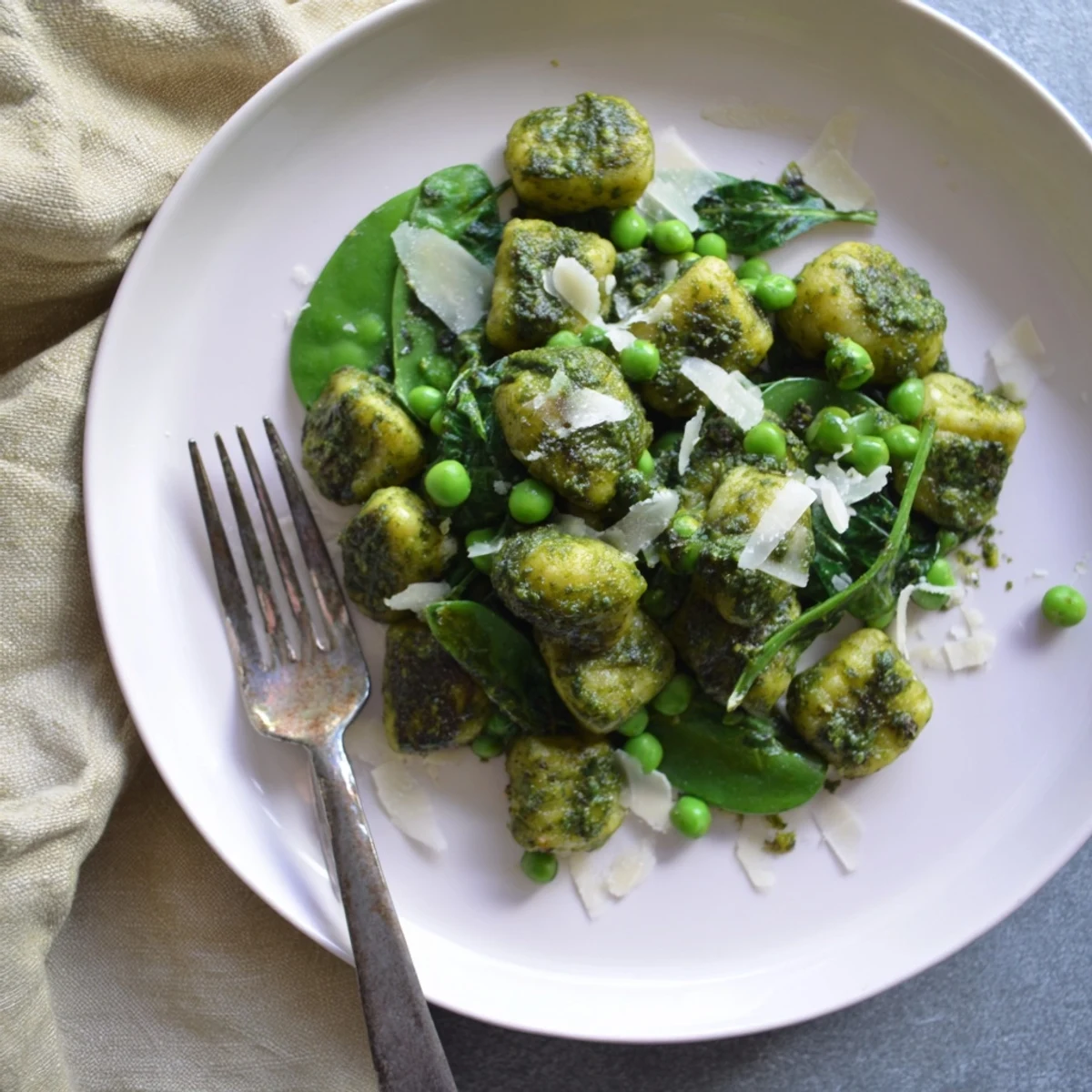 Golden-brown pan-fried gnocchi and vibrant green peas tossed in a glossy, aromatic basil pesto sauce in a hot skillet.