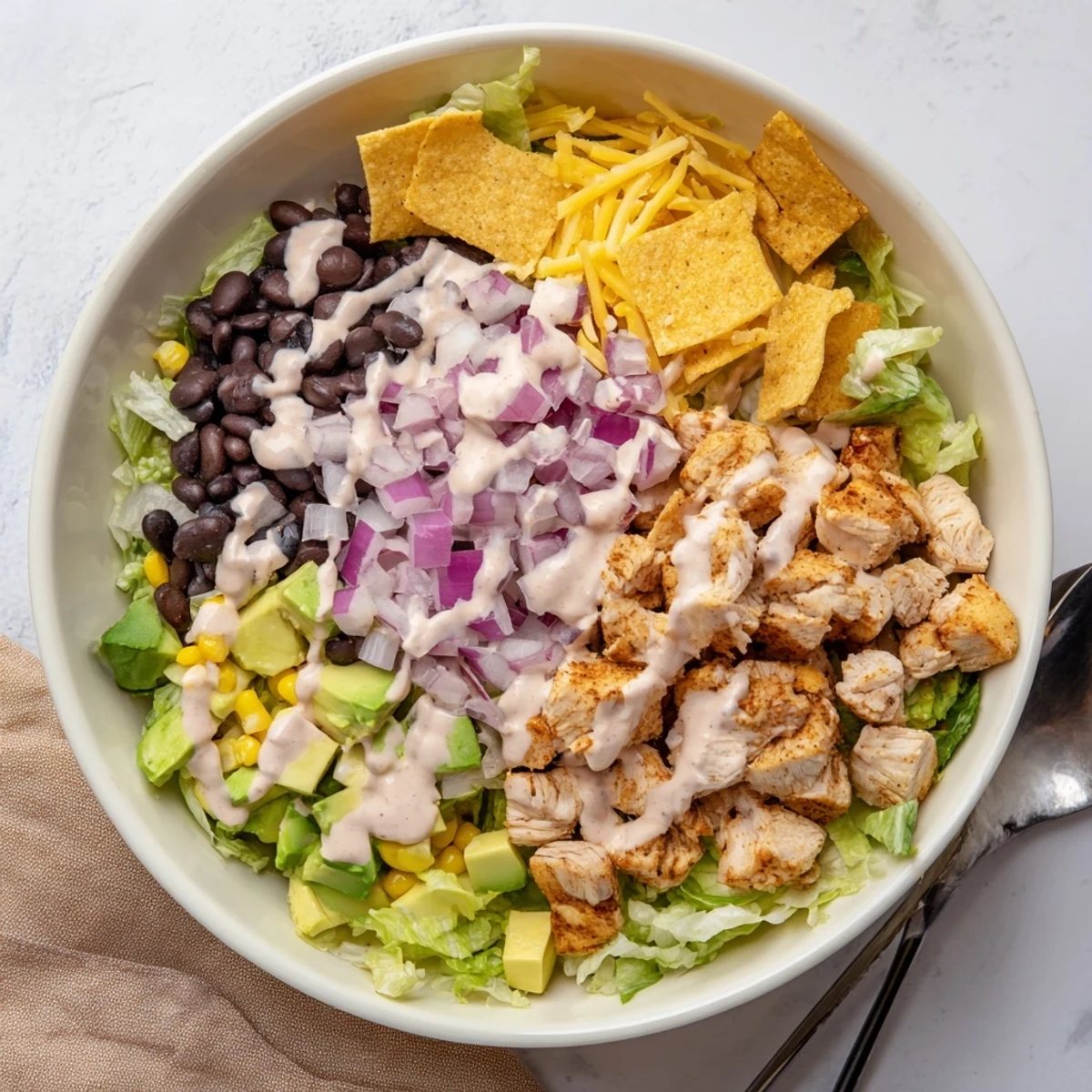 Top view of a hearty Chicken Taco Chopped Salad featuring black beans, corn, and crushed tortilla chips on fresh greens.