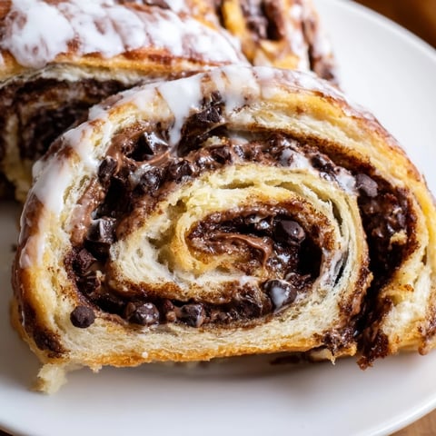 Freshly baked Nutella chocolate chip rolls sit on a cooling rack, showing melted chocolate swirls through soft dough.  