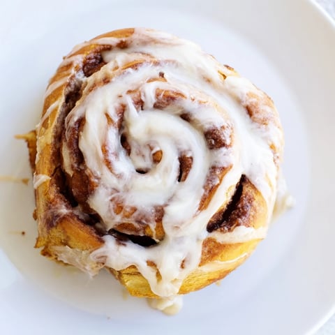Freshly baked Pillow Soft Cinnamon Rolls with creamy glaze, served warm on a rustic wooden table.  