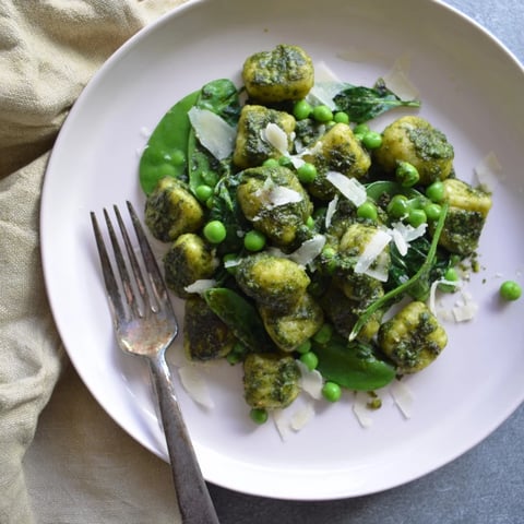 Golden-brown pan-fried gnocchi and vibrant green peas tossed in a glossy, aromatic basil pesto sauce in a hot skillet.