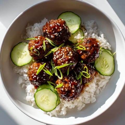 A close-up of savory teriyaki meatball bowls, showcasing the vibrant cucumber and sesame seed toppings.