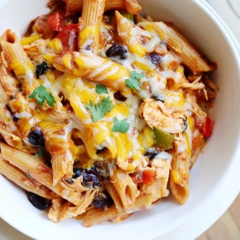 Two servings of cheesy Chicken Enchilada Pasta on a plate, with extra sour cream and diced avocado on the side.