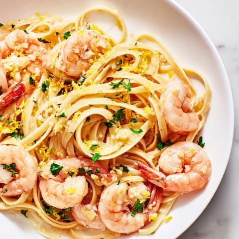 Freshly chopped parsley and a sprinkle of grated Parmesan cheese garnish this warm, steaming plate of Garlic Butter Shrimp Linguine, perfect for a quick weeknight Italian-American dinner.