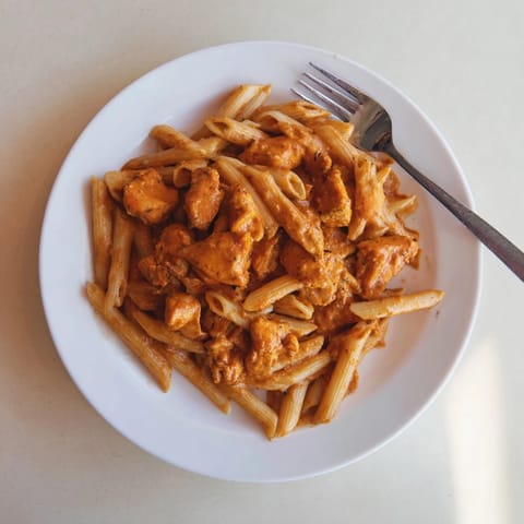 Steaming Chicken Tikka Pasta served in a white bowl, highlighting the vibrant tomato cream sauce.