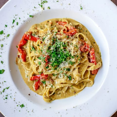 A close-up of creamy Cajun pasta topped with grated Parmesan, showcasing vibrant roasted bell peppers and a velvety, Cajun-spiced cream sauce.  
