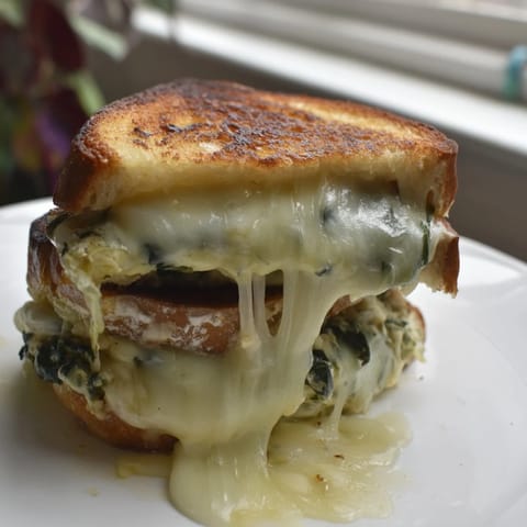 The Artichoke Spinach Grilled Cheese sandwich reveals a creamy, warm filling speckled with greens on a golden crust.  