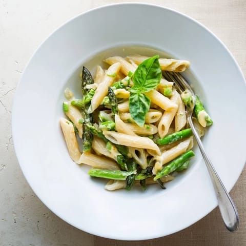 A close-up of Garlic Parmesan Spring Vegetable Pasta with penne, bright green asparagus, peas, and green beans in a creamy sauce, topped with fresh basil.  