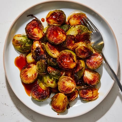 Golden roasted Brussels sprouts with a glistening balsamic reduction drizzle, served on a white plate for a savory side dish.